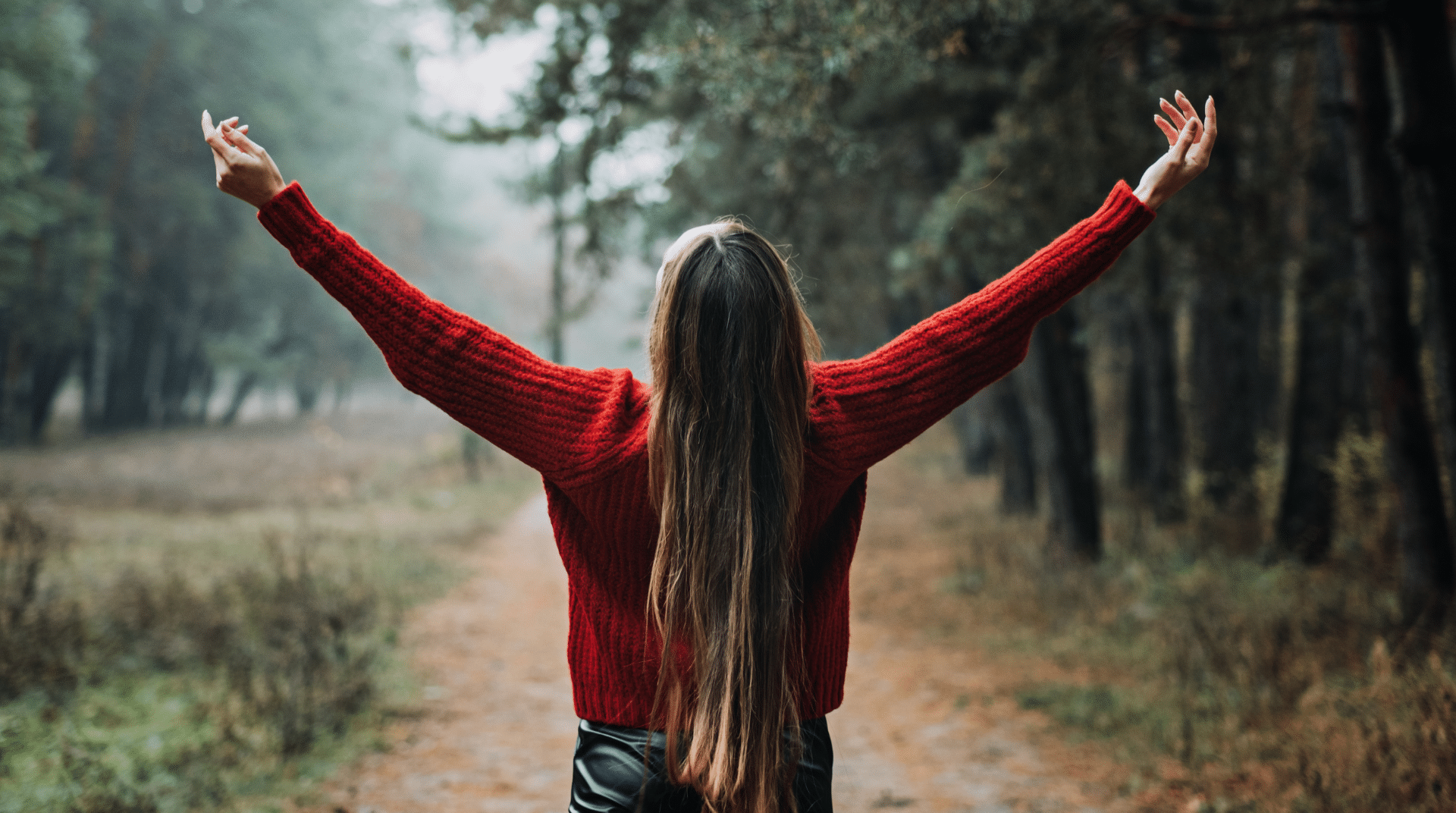 woman on a wooded trail with arms reaching up to the sky representing the benefits of emotional wellness